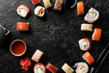 Frame made of tasty sushi rolls with chopsticks, teapot and cup of tea on black grunge background
