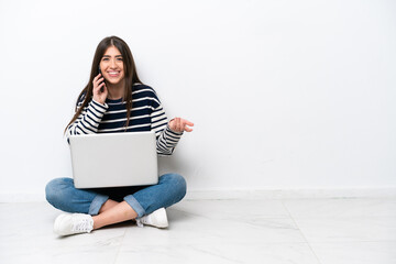 Young caucasian woman with a laptop sitting on the floor isolated on white background keeping a...