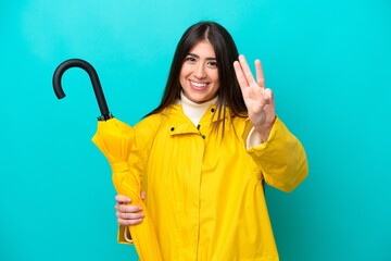 Young caucasian woman with rainproof coat and umbrella isolated on blue background happy and...