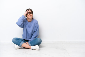 Young caucasian woman sitting on the floor isolated on white background looking far away with hand to look something