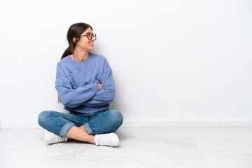 Young caucasian woman sitting on the floor isolated on white background in lateral position