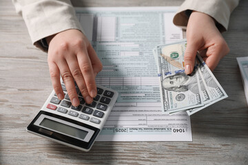Payroll. Woman with dollar banknotes and calculator planning budget at wooden table, closeup
