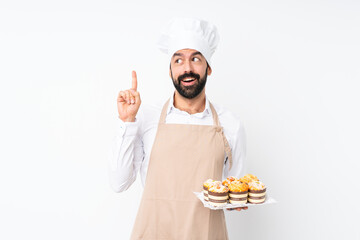 Young man holding muffin cake over isolated white background thinking an idea pointing the finger up