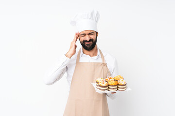 Young man holding muffin cake over isolated white background with headache