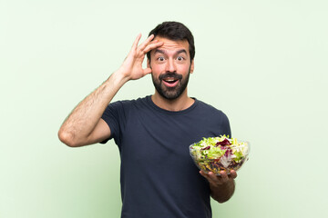 Young handsome man with salad over isolated green wall has just realized something and has intending the solution