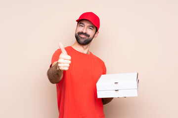 Young man holding a pizza over isolated background with thumbs up because something good has happened