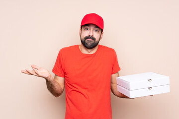 Young man holding a pizza over isolated background making doubts gesture