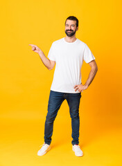 Full-length shot of man with beard over isolated yellow background pointing finger to the side