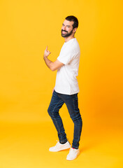 Full-length shot of man with beard over isolated yellow background pointing back