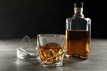 Alcohol addiction. Whiskey in glass, bottle, cigarettes and ashtray on wooden table