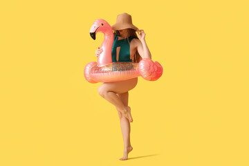 Beautiful young happy woman in swimsuit with inflatable ring on yellow background
