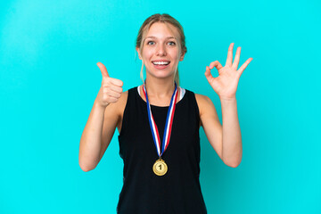 Young caucasian woman with medals isolated on blue background showing ok sign and thumb up gesture