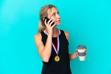 Young caucasian woman with medals isolated on blue background holding coffee to take away and a...