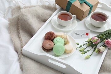 Tasty breakfast served in bed. Delicious macarons, tea, gift box, flowers and I Love You card on tray