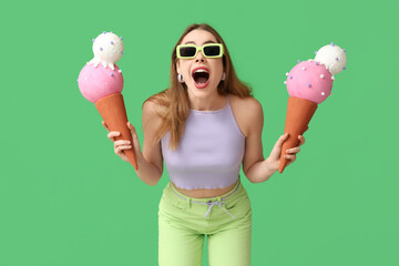 Surprised young woman holding toy ice creams on green background