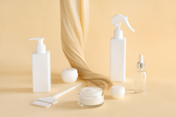 Blonde strand with jars of hair mask, brush and bottles of cosmetic products on yellow background