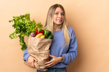 Young blonde woman holding a bag full of vegetables over isolated background having doubts and with...