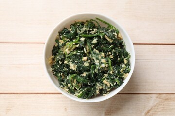 Tasty spinach dip with eggs in bowl on light wooden table, top view