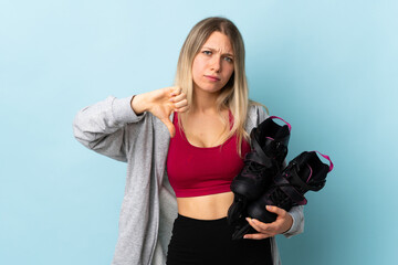 Young blonde woman holding a roller skates isolated on pink background showing thumb down sign