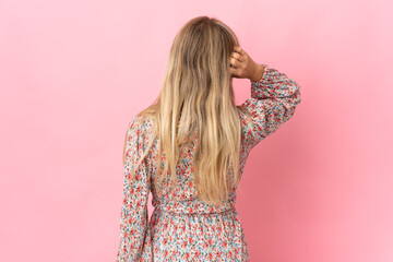 Young blonde woman isolated on pink background in back position and thinking