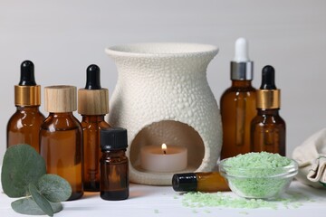 Different aromatherapy products, burning candle and eucalyptus leaves on white wooden table against...