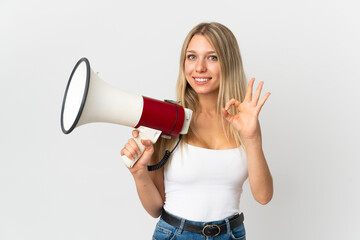 Young blonde woman isolated on white background holding a megaphone and showing ok sign with fingers