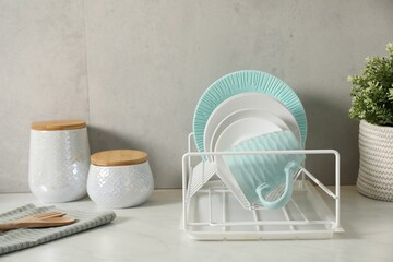 Drainer with different clean dishware and cup on light table indoors