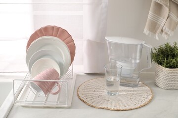 Drainer with different clean dishware, glass and cup on light table indoors