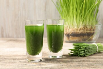 Wheat grass drink in shot glasses and fresh green sprouts on wooden table, closeup