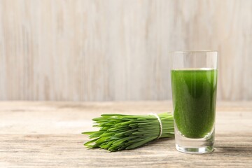 Wheat grass drink in shot glass and fresh green sprouts on wooden table, closeup. Space for text