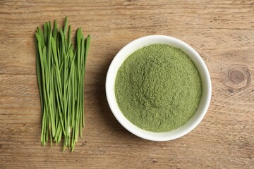 Wheat grass powder in bowl and fresh green sprouts on wooden table, flat lay