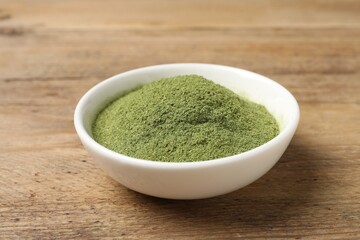 Wheat grass powder in bowl on wooden table, closeup