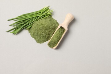 Pile of wheat grass powder, scoop and fresh sprouts on light grey table, flat lay. Space for text