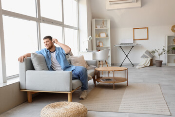 Young bearded man in headphones listening to music on couch at home