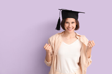 Happy female student in graduation hat showing yes gesture on lilac background