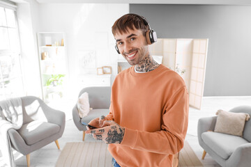Young tattooed man in headphones with mobile phone listening to music at home