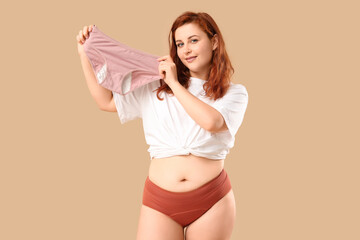 Young woman holding period panties on beige background