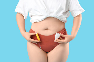Young woman in period panties holding menstrual cup with tampon on blue background