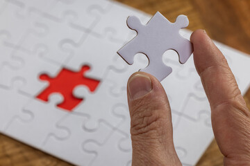 Blank puzzle with the missing piece being held next to the whole with a red placer where the last...