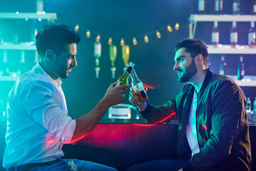 Men, pub and toast with beer bottle in club, bar and rave for party or cheers. People, friends and salute with alcohol for downtime from work at event, festival and nightclub in the city at night