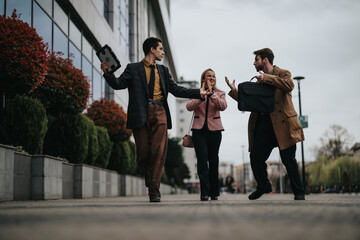 Three young business professionals jovially walking outside a modern building, engaging in a light-hearted conversation.