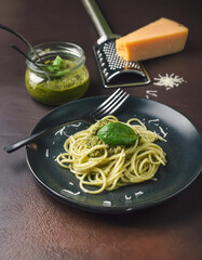 A tantalizing plate of spaghetti with pesto, garnished with fresh basil leaves, next to a block of cheese and a jar of pesto sauce