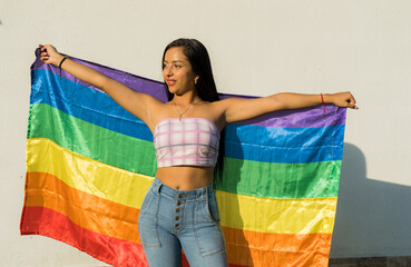 mujer joven con sus brazos abiertos sosteniendo la bandera LGBTIQ+