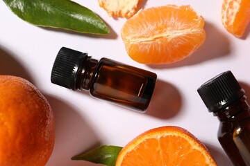 Aromatic tangerine essential oil in bottles and citrus fruits on white table, flat lay
