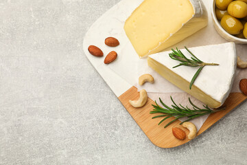 Pieces of tasty camembert cheese, rosemary, nuts and olives on grey textured table, top view. Space...