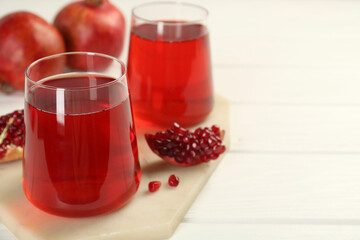 Tasty pomegranate juice in glasses and fresh fruits on white wooden table, closeup. Space for text