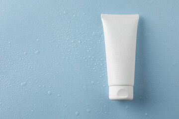 Moisturizing cream in tube on light blue background with water drops, top view. Space for text