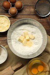 Flat lay composition with fresh butter and flour in bowl among other products on wooden table