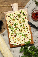 Fresh butter board with cut olives, sun-dried tomatoes, bread and knife on wooden table, flat lay