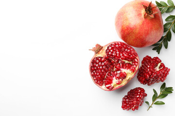Fresh pomegranates and green leaves on white background, flat lay. Space for text
